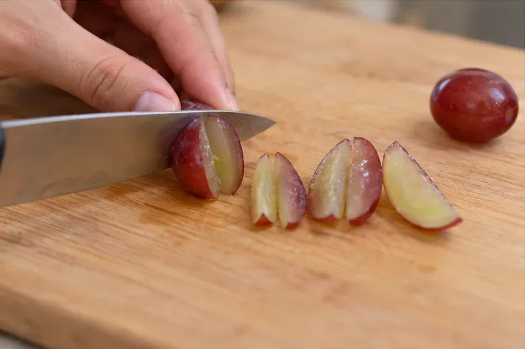 A caregiver cutting a grape lengthwise into narrow pieces on a wooden cutting board