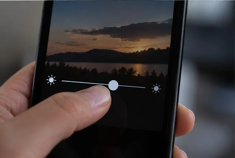 A thumb adjusts a brightness slider on a phone camera preview